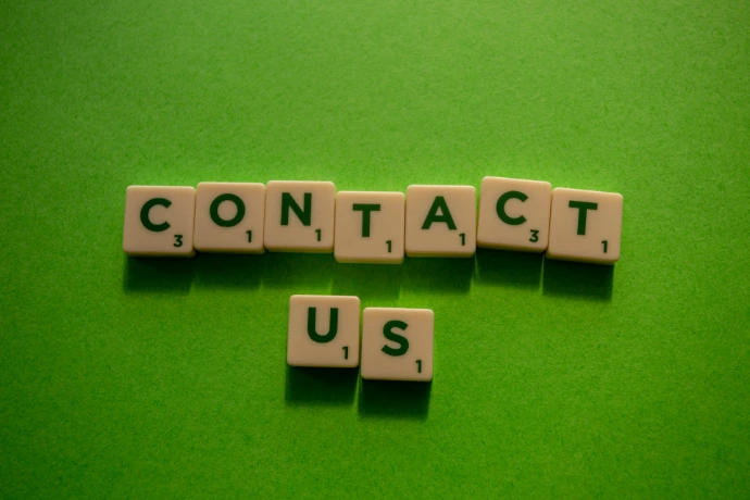 Scrabble tiles spelling contact us on a solid green background